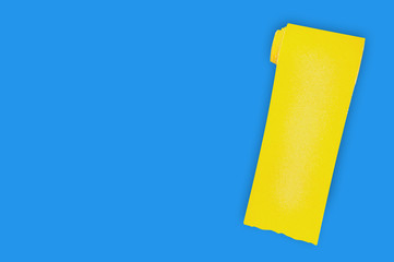 One new roll of yellow abrasive sandpaper for grid wood or metal items on blue table in workshop. Copy space for your text. Top view. Building or repair concept