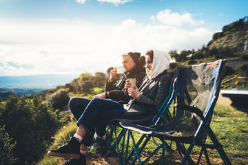 love couple sit in camping chairs on top of sun flare mountain, travelers drink tea on cup enjoy...