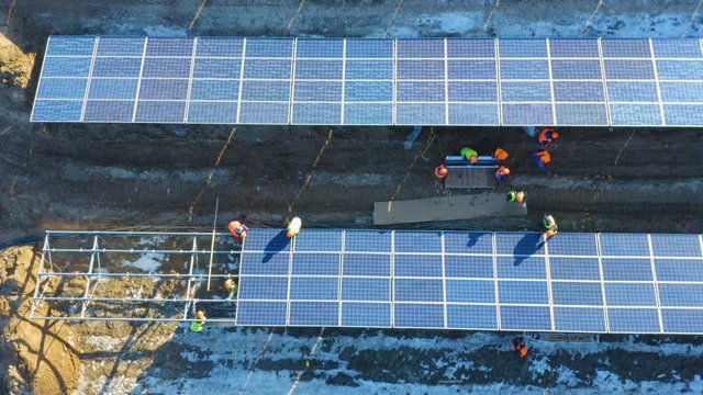 Aerial top view of a group of electricians  in bright helmets installing solar panels at a solar power plant under construction