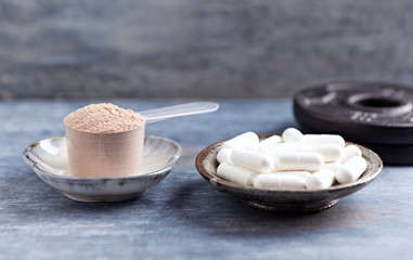 Creatine capsules, Scoop of Whey Protein and plates. Nutrition for bodybuilding. Fitness supplements on rustic wooden background. Close up. Copy space