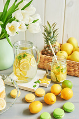 Lemonade and flowers tulips on table. Mason jar glass of lemonade with lemons and straw. Copy space. Fruits and macaroons on the table. The concept of spring and summer season.Healthy Food and Drink