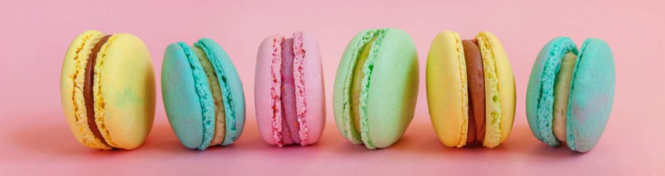 Sweet almond colorful unicorn pink blue yellow green macaron or macaroon dessert cake isolated on trendy pink pastel background. French sweet cookie. Minimal food bakery concept. Banner