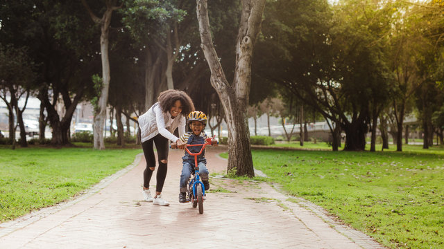 Little boy learning to ride bicycle at park with mother