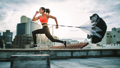 Woman running on rooftop with a resistance parachute - obrazy, fototapety, plakaty
