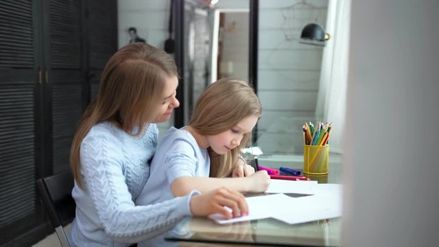 Caring young mother helping little daughter drawing picture using colorful pencil medium shot
