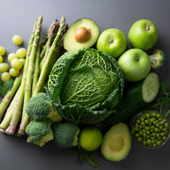 Raw healthy food clean eating vegetables: asparagus, cucumber, basil, green peas, avocado, broccoli, lime, apples, grapes, broccoli on dark background, top view. Square image.