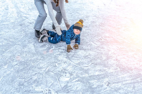 Young mother woman raises son boy 4-6 years ice in winter in city park. The concept of first lesson on skating support and support, help of parents in learning sports activities and active lifestyle.