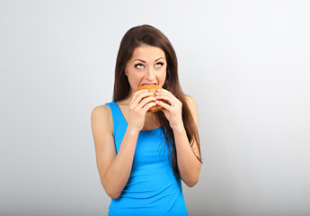 Excited happy fun hungry woman biting tasty burger and looking up on blue background. Closeup portrait