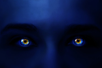 Creative photo of a woman's face with neon light dark blue color and glowing multi-colored eyes with a mysterious intense look. Glowing in the dark eyes close-up macro.