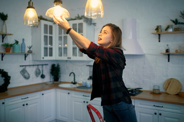 Young woman changing a light bulb at the kitchen