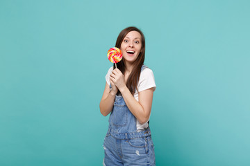 Portrait of surprised excited young woman in denim clothes keeping mouth open, holding colorful...