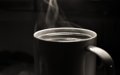 White cup with a hot drink tea or coffee with smoke or steam on a dark background. selective focus