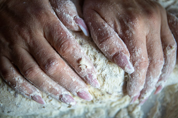 Woman's hands with manicured nails work with dough in the kitchen. Kneading homemade dough with flour for bread, pastry or pizza.