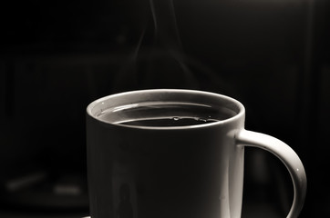 White cup with a hot drink tea or coffee with smoke or steam on a dark background. selective focus