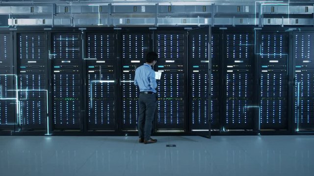 The Concept of Digitalization of Information: IT Specialist Standing In front of Server Racks with Laptop, He Activates Data Center with a Touch Gesture. Animated Visualization of Network