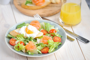 Green salad with lightly salted salmon. On a plate with salad toast with poached egg. In the frame of a glass with orange juice and a plate with bruscheta. Light background. Close-up. Macro shooting. 