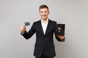 Smiling young business man in classic suit holding credit bank card, metal bank safe for money accumulation isolated on grey background. Achievement career wealth business concept. Mock up copy space.