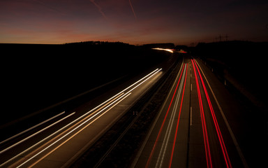 Obraz premium Night urban scene of motion blurred light tracks glowing to the darkness of highway traffic transport to the city just after sunset. Creative long time exposure diagonal composed photography.