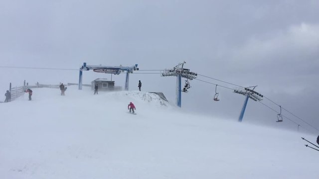 Ski chairlift at a ski resort filmed during a strong wind surrounded by a large number of skiers and snowboarders