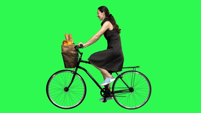 Happy woman riding a bicycle over a green screen,  looking upwards impressed., waving hello. No motion blur for optimal keying.