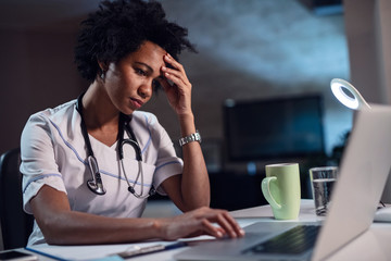 African American female doctor with headache working on laptop.