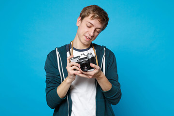 Portrait of young man in casual clothes holding taking pictures on retro vintage photo camera isolated on blue wall background in studio. People sincere emotions lifestyle concept. Mock up copy space.