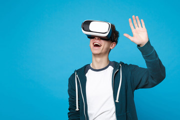 Smiling young man in casual clothes looking on headset waving and greeting with hand isolated on blue wall background. People sincere emotions, lifestyle concept. Mock up copy space. Advertising area.