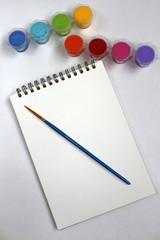 A blank pad of paper with paints and a paint brush