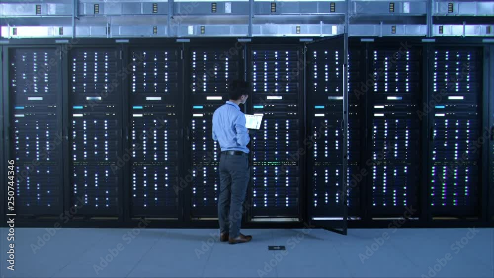 Poster IT Specialist Standing In front of Server Racks with Laptop, He Activates Data Center with a Touch Gesture. Turning On New Data Center.