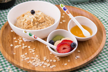 In the bowl breakfast oatmeal, mixed fresh fruit, and honey on wood table