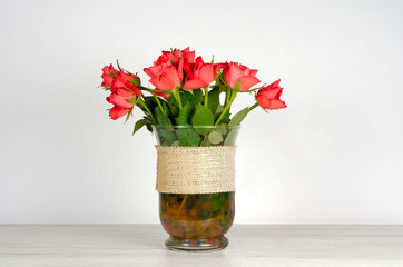 Close-up of red  roses in a   transparent vase  sitting on a white furniture against white background