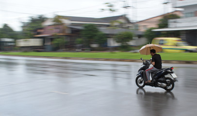 Yala, Thailand, November, 19, 2018 :Motion Blurred panning photo of man riding motorcycle in the rain on road and holding umbrella,raining season
