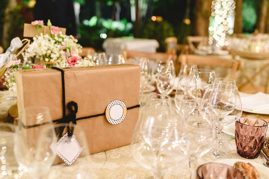 Gift box wrapped in paper and with bow and empty label to include free text, on the elegant table of the reception of a wedding, without anyone.