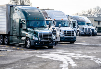 Big rigs long haul semi trucks stand on the truck stop parking for truck drivers rest