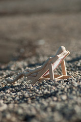 closeup of wooden mannequin in wooden lounge chairon pebbles beach