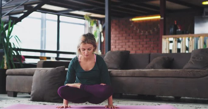 Hard yoga poses blonde lady practicing in the morning at home in the living room she standing in her hands and have a crossed legs healthy lifestyle , arm balance exercises