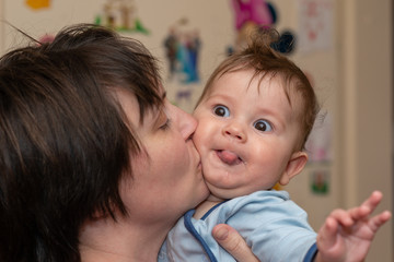 Mother kisses a beautiful male baby which shows the tongue