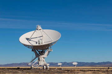 Very Large Array radio antenna dish close with others in distance, blue sky copy space, horizontal aspect