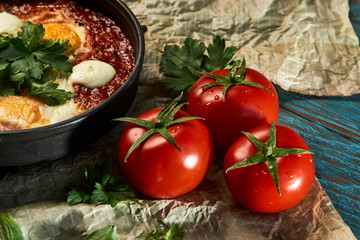 Hot shakshuka with eggs, tomatoes and parsley in a frying pan, close-up