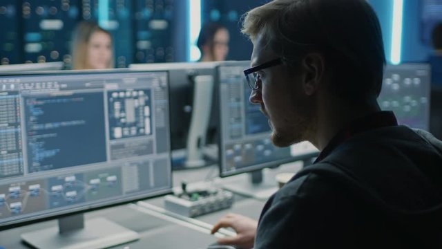 Smart Male IT Programer Working on Desktop Computer in Data Center Technical System Control Room. Team of Young Professionals Programming in Coding Language