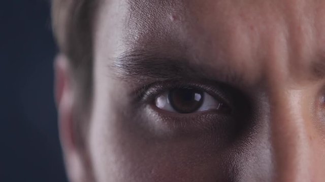 Close up Brown eye of young caucasian man opening his eye and looking into camera lens on black misty background.