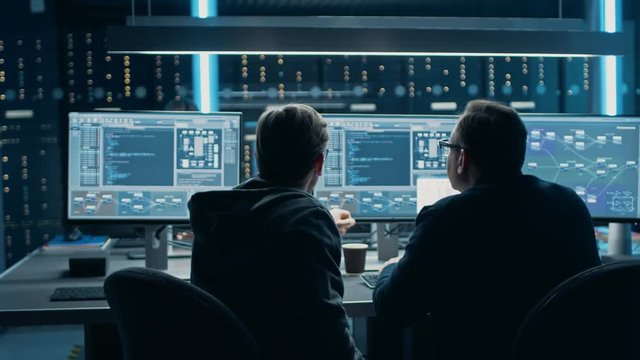 Two Professional IT Programers Discussing Blockchain Data Network Architecture Design and Development Shown on Desktop Computer Display. Working Data Center Technical Department with Server Racks 