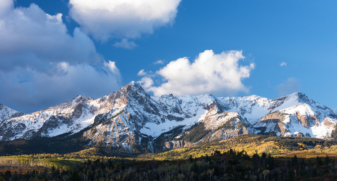 Mount Sneffels is within the Uncompahgre National Forest. An early fall snowstorm covers the mountain range  with aspen groves in full colo