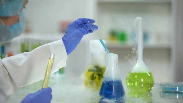 Scientist adding blue liquid in tube with yellow oily substance, biofuel testing