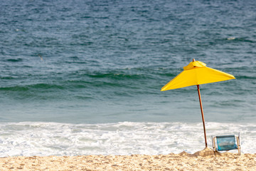yellow sun umbrella and chair on a beautiful sunny day on the beach with the clear blue sea in the background