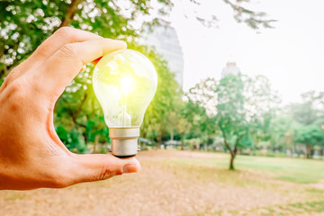 Human holding light bulb and blur green nature at the park , concept protect the environment.
