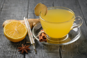 Ginger drink to boost immunity and a thermometer to measure body temperature on a black table.