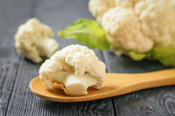 Inflorescence of cauliflower in a wooden spoon on a dark black table.