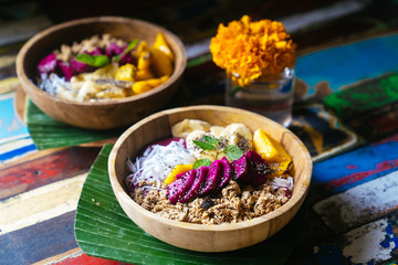 Close up four smoothie bowls made with mango, banana, granola, grated coconut, dragon fruit, chia seeds and mint on colored background