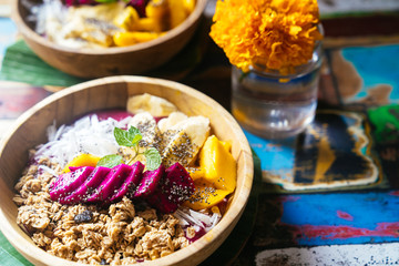 Close up four smoothie bowls made with mango, banana, granola, grated coconut, dragon fruit, chia seeds and mint on colored background